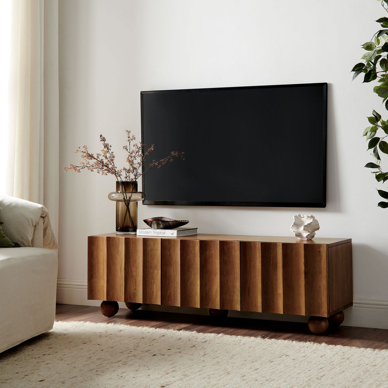 Walnut wood TV stand styled under a wall-mounted TV with decor accents and rounded bun feet || EEI-7183-WAL || front_angle_room