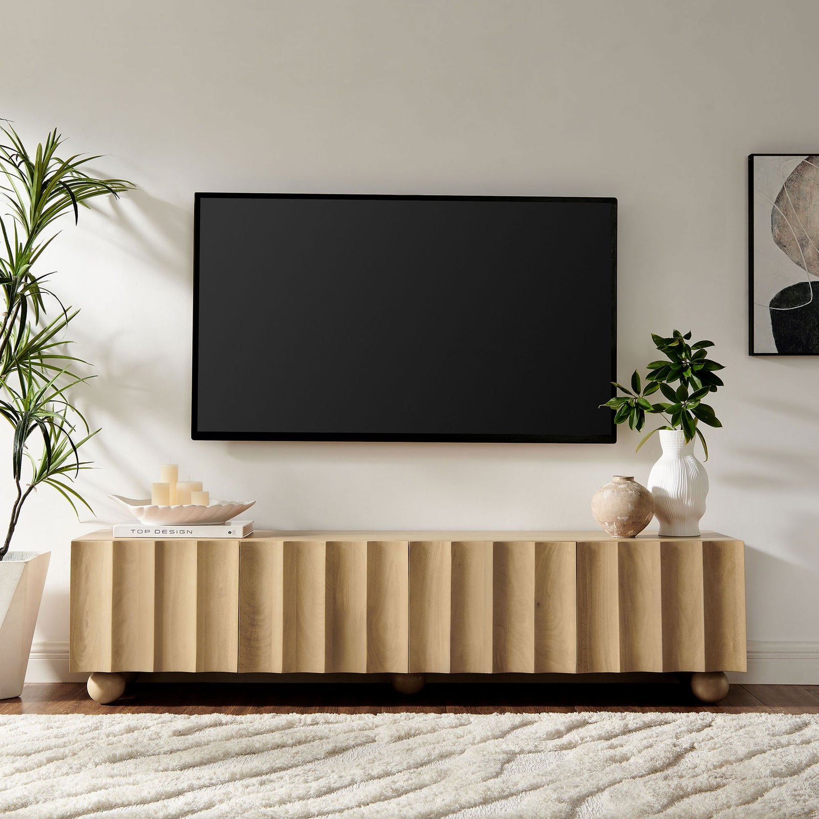Natural long TV stand styled in a living space with wall-mounted TV, rug, and sculptural decor || EEI-7184-NAT || front_angle_room