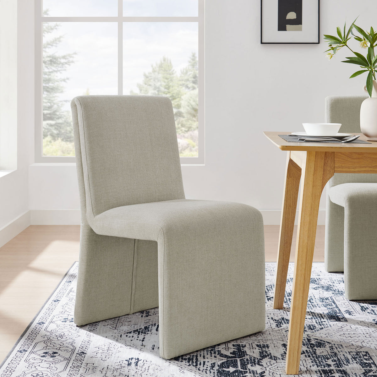 Linen slipper dining chair styled beside a modern wood table in a bright airy room || EEI-7185-LIN || front_angle_room
