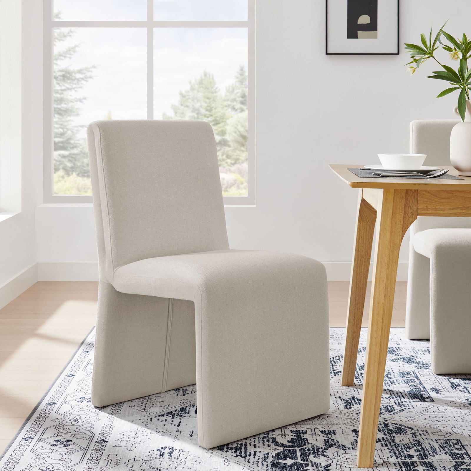 Emory upholstered dining chair in salt fabric styled beside a wooden table in a sunlit dining space || EEI-7185-SAL || front_angle_room