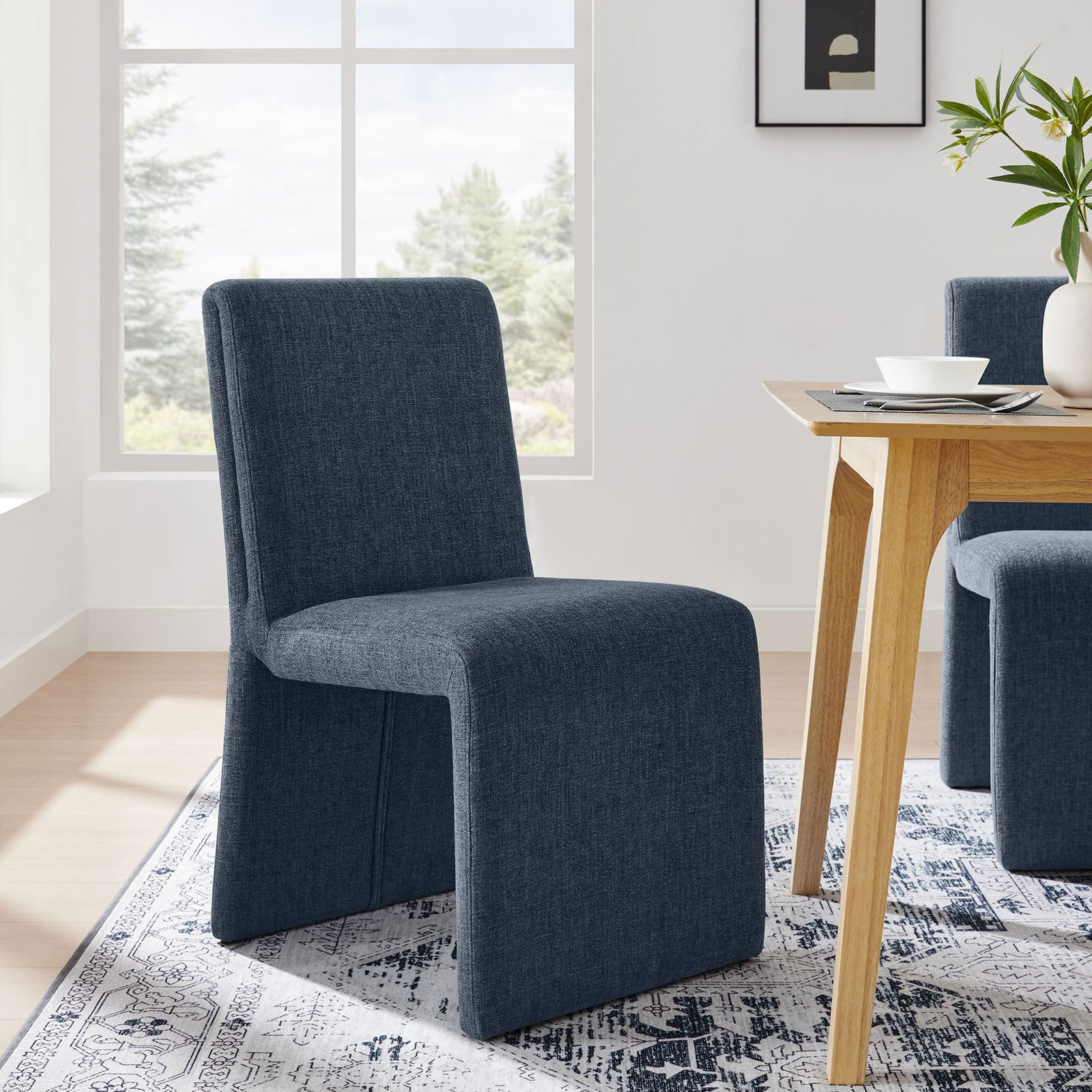Slate blue Emory dining chair styled at a modern wood table on a patterned rug in a bright room || EEI-7185-SLB || front_angle_room