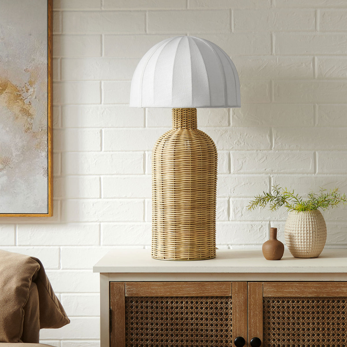 Santo rattan table lamp anchors a modern coastal vignette on a wooden cabinet against white brick || EEI-7186-WHI-NAT || front_room