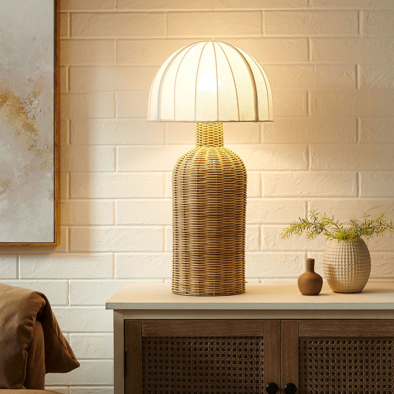 Santo rattan table lamp casts a warm ambient glow, creating cozy lighting on a bedside or console || EEI-7186-WHI-NAT || front_on_room