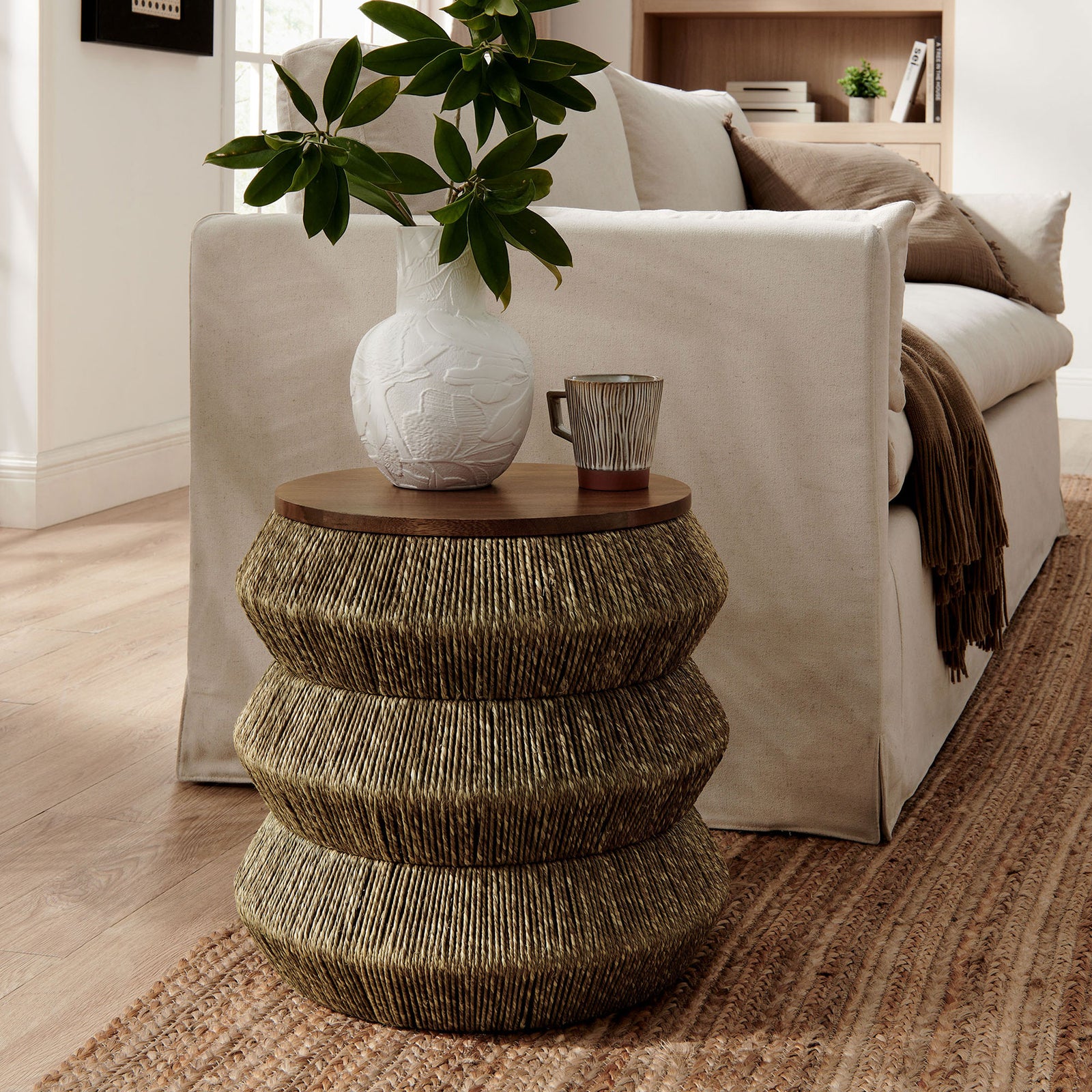 Round seagrass and wood end table beside sofa with decor accents || EEI-7188-WAL-NAT || front_angle_room