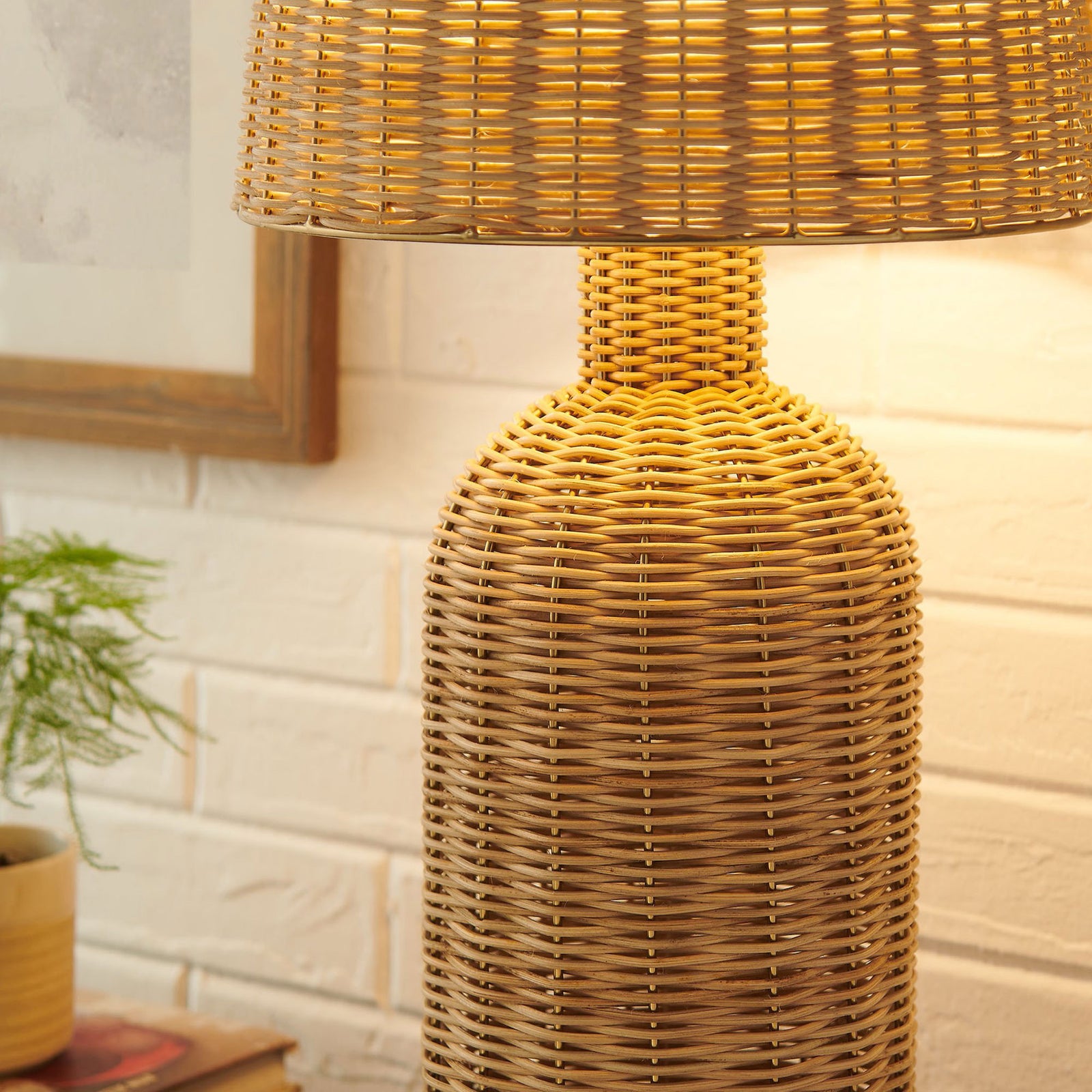 Briar rattan table lamp casting a warm glow beside decor on a textured brick wall || EEI-7191-NAT || detail_room