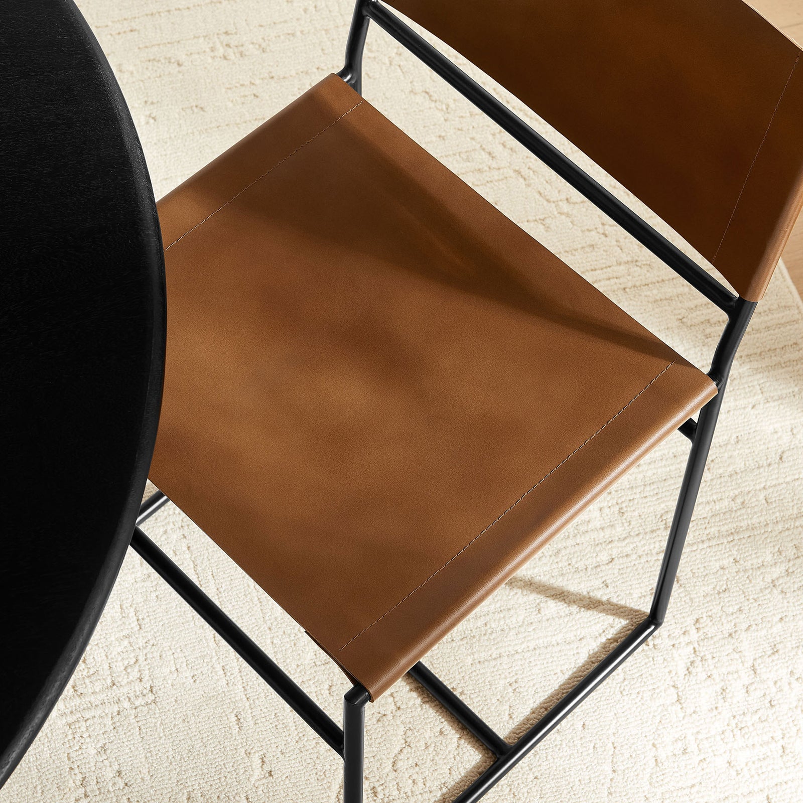 Tan leather dining chair seat over black metal frame adds warmth beside a dark table and light rug || EEI-7196-TAN || detail_room