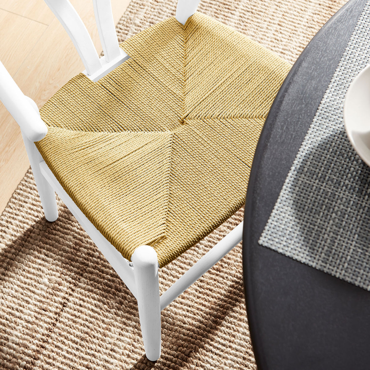 Natural rope seat and white wood frame styled beside a round dining table on a woven area rug. || EEI-7200-WHI || detail_room