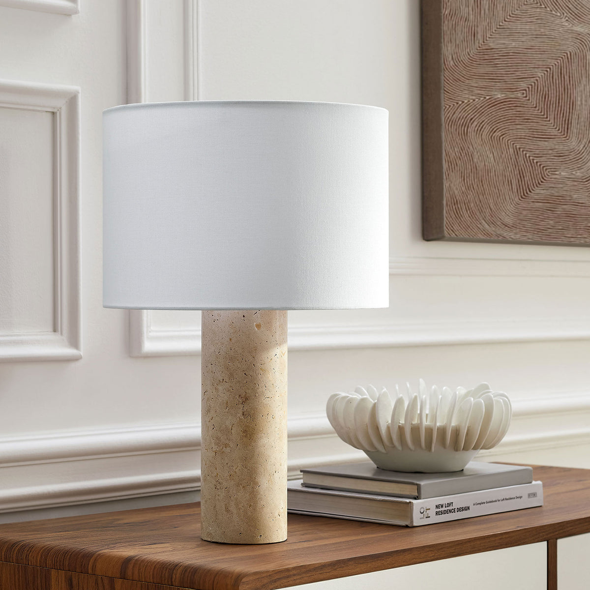 Zenith travertine table lamp with white shade styled on a console in a bright modern room || EEI-7213-TRV || front_angle_room