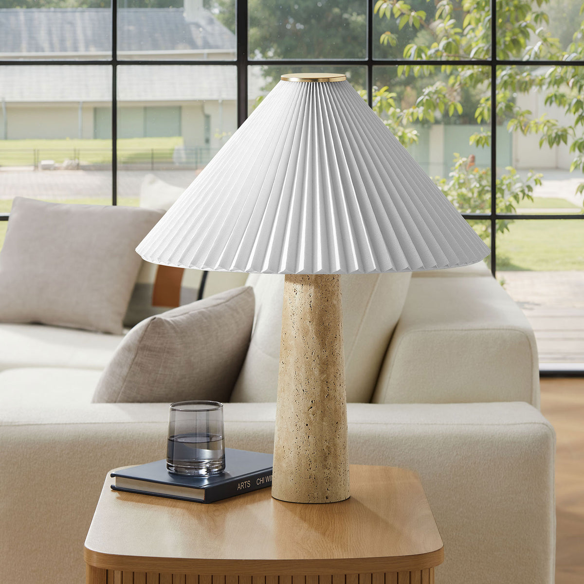 Cove table lamp sits on a wood side table, pairing its travertine base with a soft white pleated shade || EEI-7215-TRV || front_room