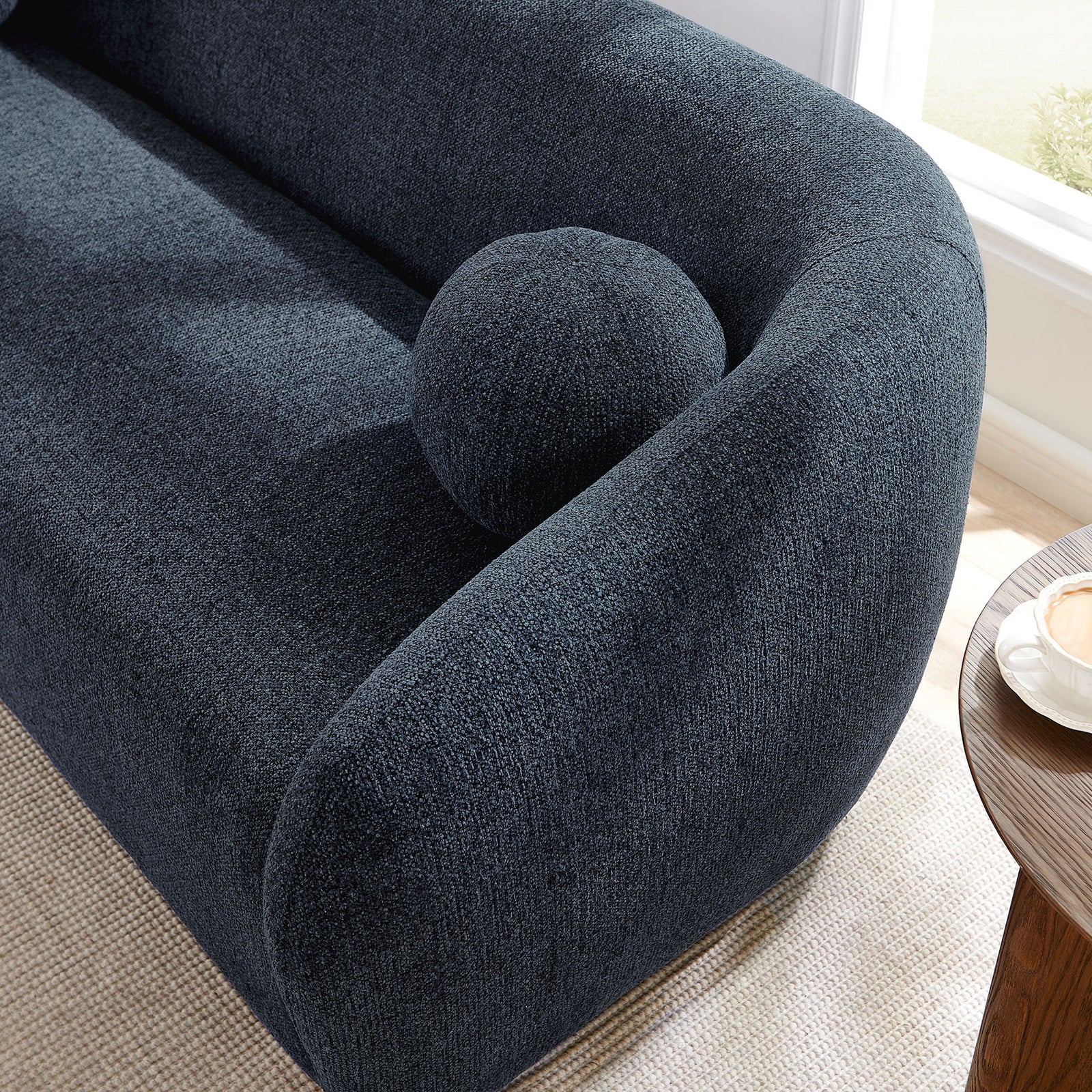 Detail of the sofa arm and ball pillow styled in a bright living room with soft natural light. || EEI-7217-NAV || detail_room