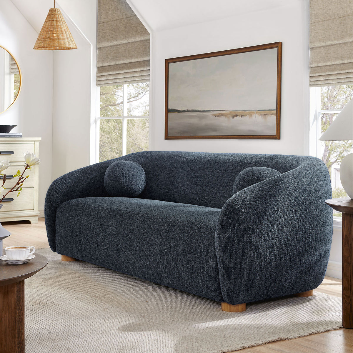 Navy curved Holland sofa styled in a modern living room with artwork, wood accents, and neutral rug. || EEI-7217-NAV || front_angle_room