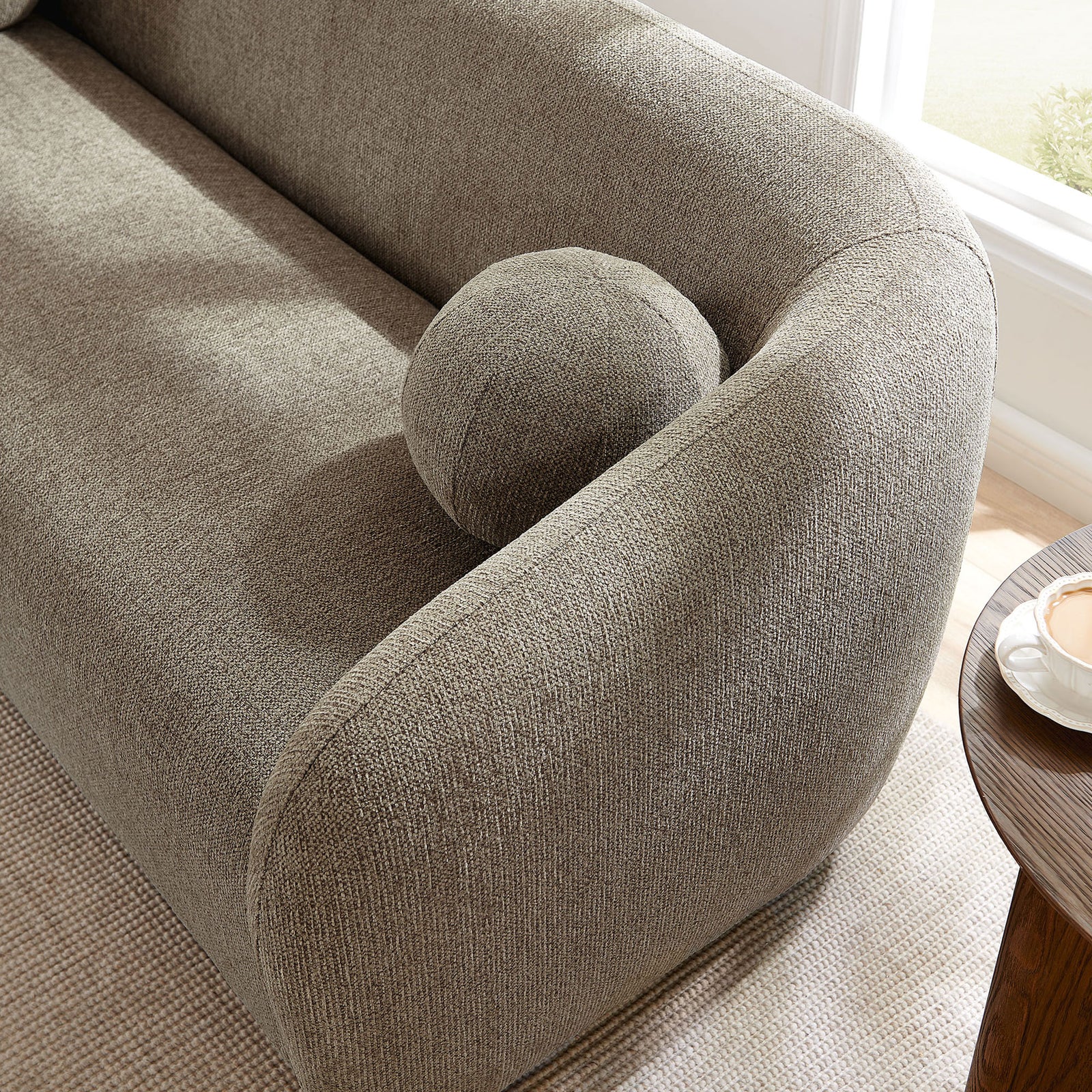 Ball pillow rests on the curved sofa arm in a bright living room with natural light and layered neutrals || EEI-7217-TAU || detail_room