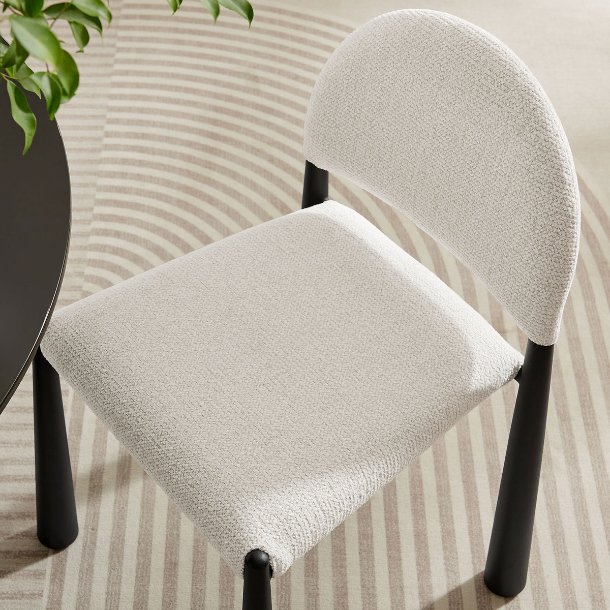 Cream boucle dining chair tucks beside a round table, showcasing its contoured seat against a patterned area rug || EEI-7220-BLK-CRE || detail_room