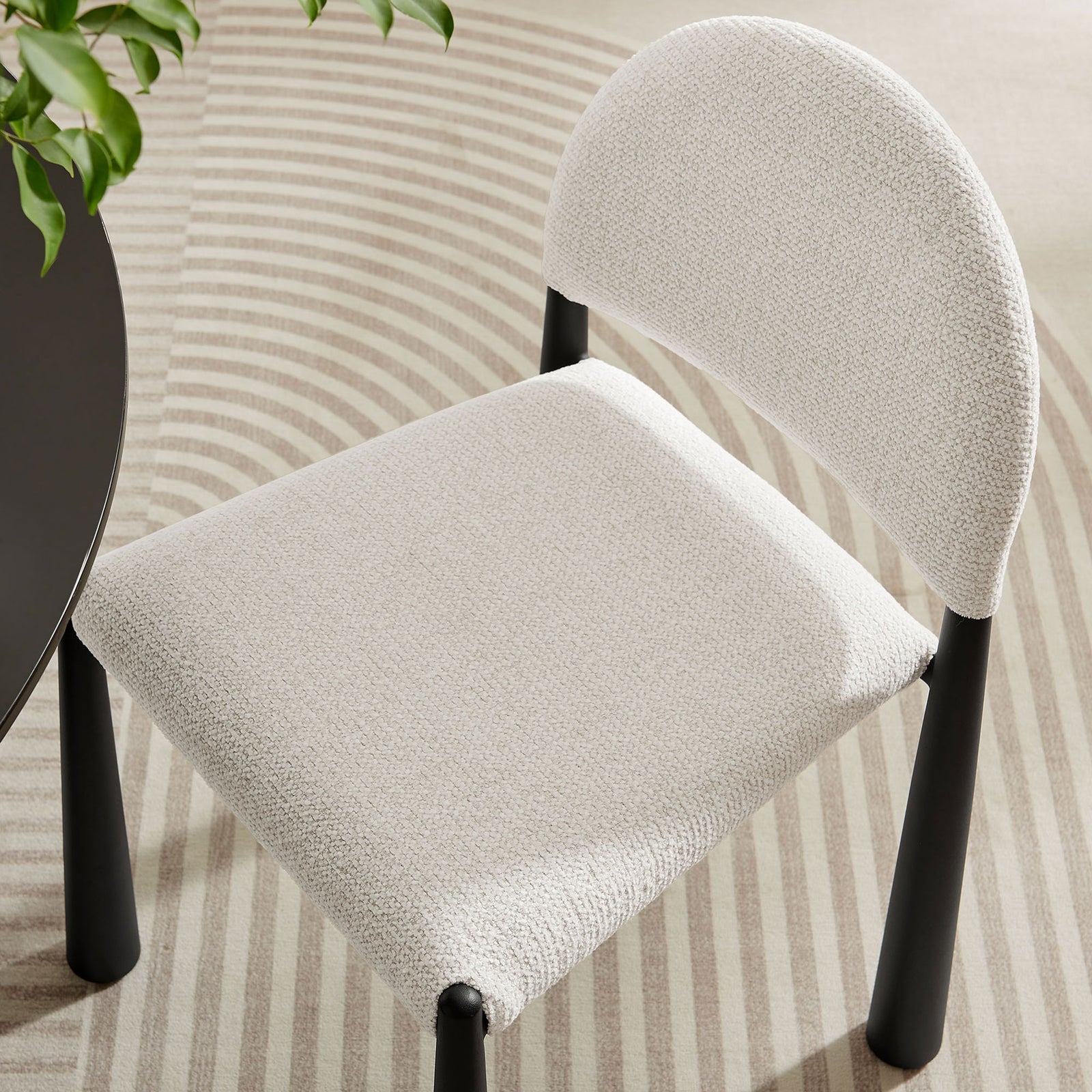 Cream boucle dining chair tucks beside a round table, showcasing its contoured seat against a patterned area rug || EEI-7220-BLK-CRE || detail_room