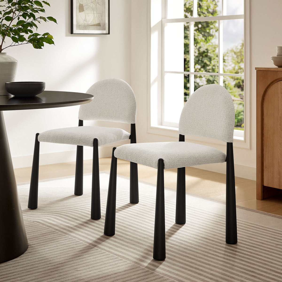 Pair of cream boucle dining chairs with black tapered legs styled in a bright modern dining room with round table || EEI-7220-BLK-CRE || front_angle_room