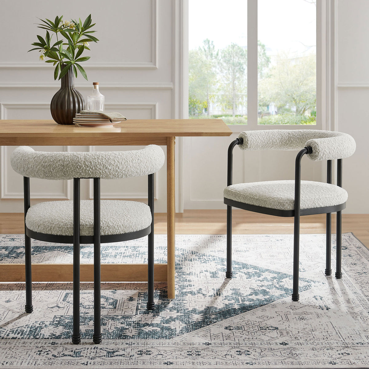 Pair of curved boucle dining chairs with black metal frames styled around a warm wood dining table || EEI-7225-BLK-PRL || front_angle_room