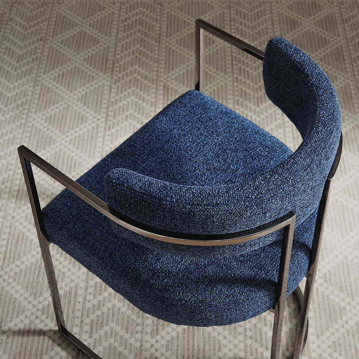 Curved navy dining chair with chrome frame styled on a patterned neutral area rug. || EEI-7228-SLV-NAV || top_angle_room