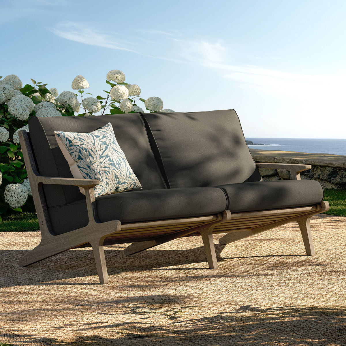 Saratoga teak loveseat styled on a coastal patio with deep flint gray cushions for relaxed lounging. || EEI-7247-WGR-FLI || front_angle_room