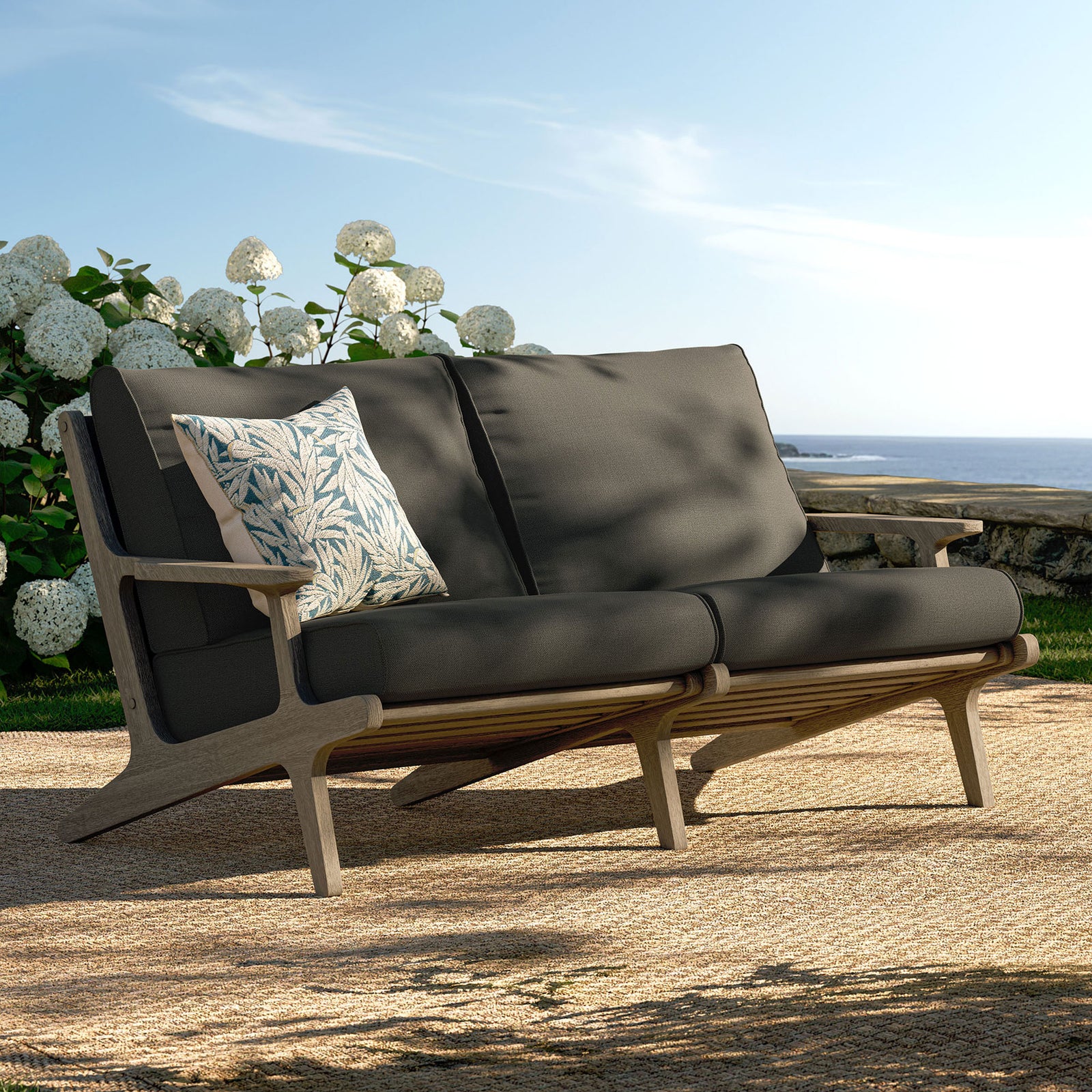 Saratoga teak loveseat styled on a coastal patio with deep flint gray cushions for relaxed lounging. || EEI-7247-WGR-FLI || front_angle_room