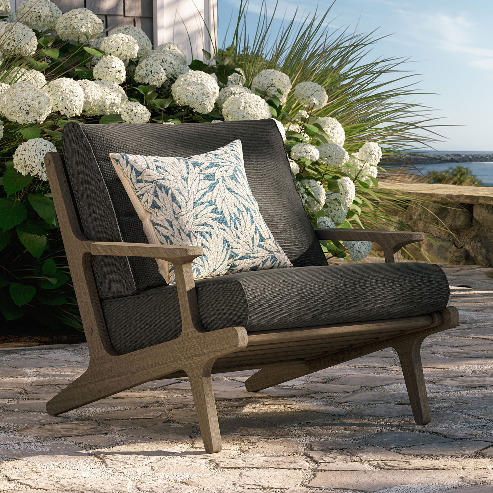 Saratoga flint gray armchair creating a welcoming teak lounge spot on a stone garden patio || EEI-7248-WGR-FLI || front_angle_room