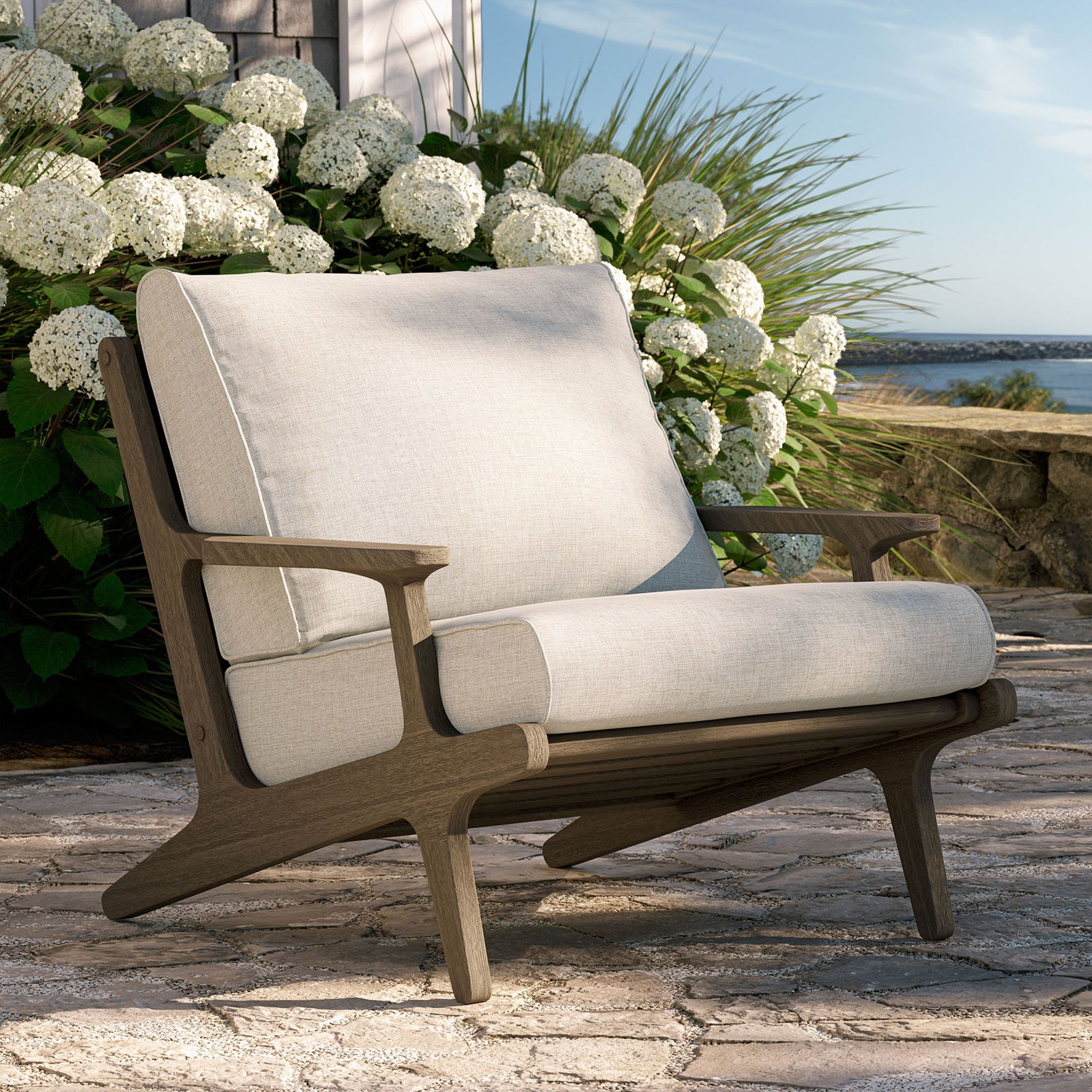 Saratoga pebble armchair creating a calm teak lounge spot on a sunlit stone patio || EEI-7248-WGR-PEB || front_angle_room