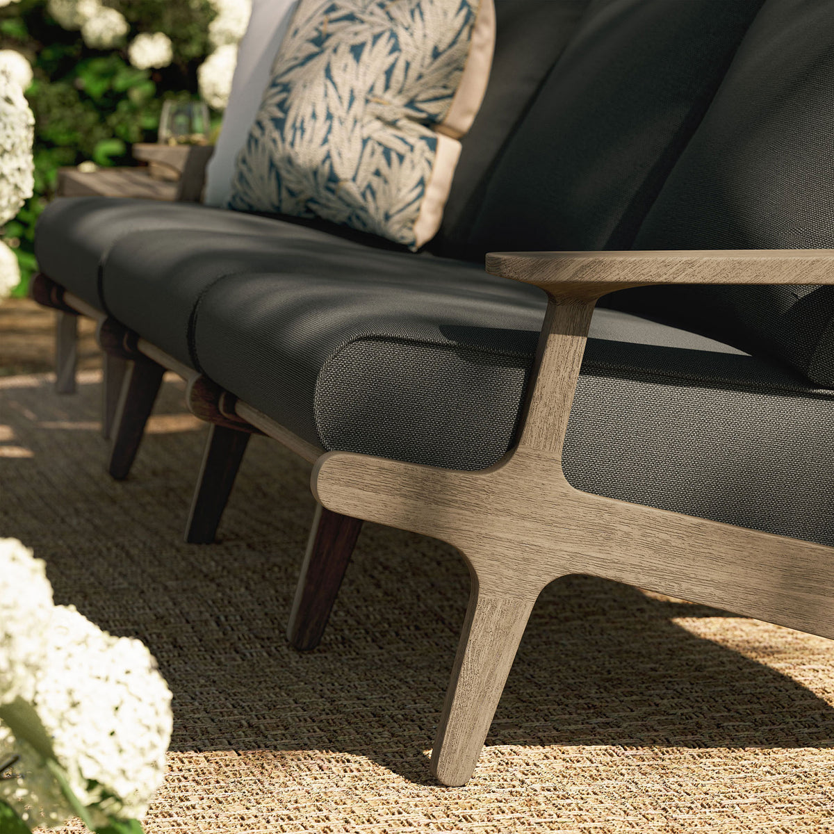 Teak outdoor sofa base resting on woven rug, paired with deep gray cushions for relaxed garden seating || EEI-7249-WGR-FLI || detail_room