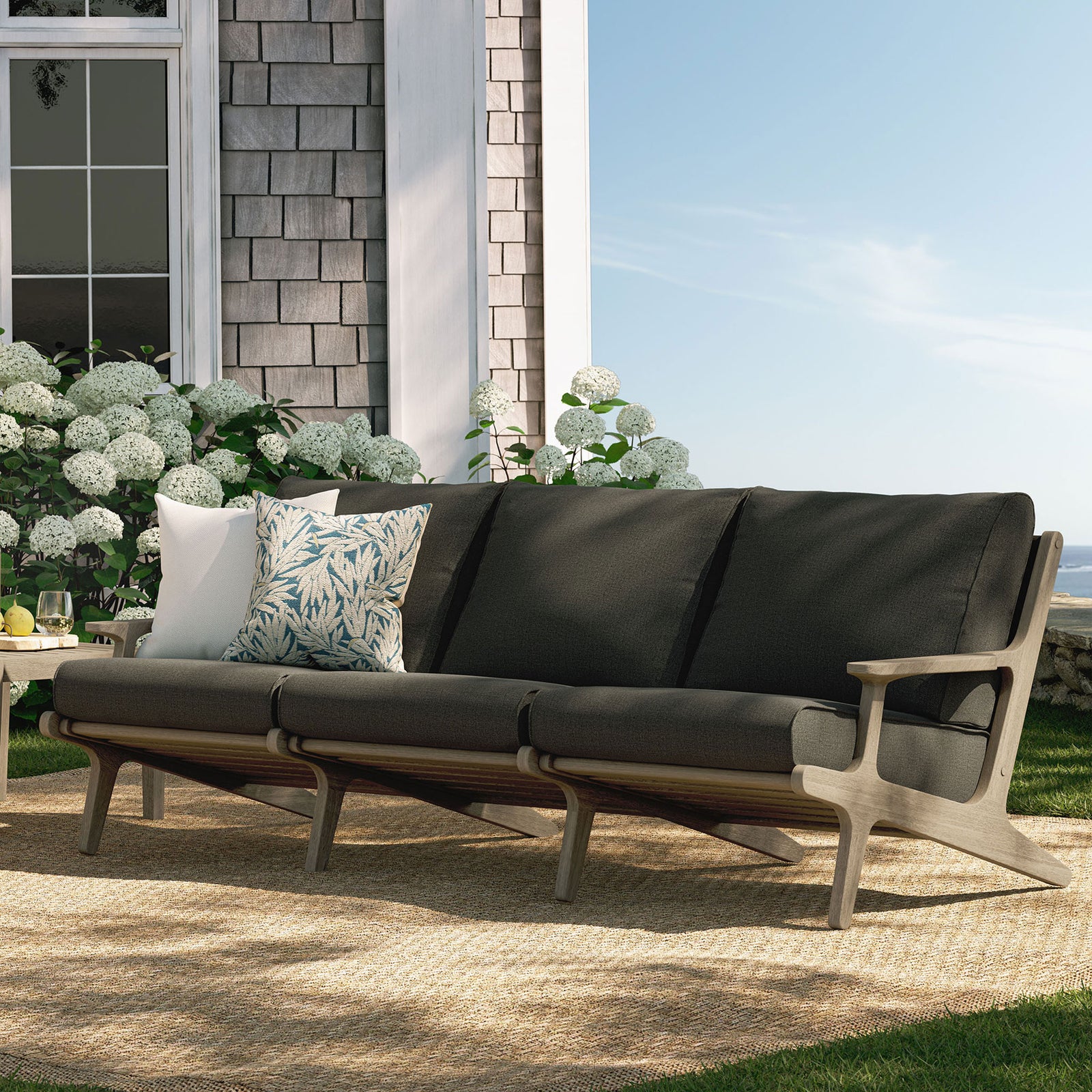 Saratoga teak sofa styled on a garden patio with flint gray cushions and accent pillows for outdoor lounging || EEI-7249-WGR-FLI || front_angle_room