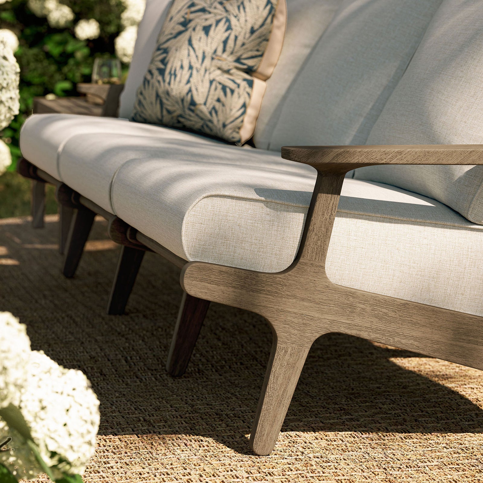 Light pebble cushions and teak legs resting on natural fiber rug in a bright garden seating area || EEI-7249-WGR-PEB || detail_room