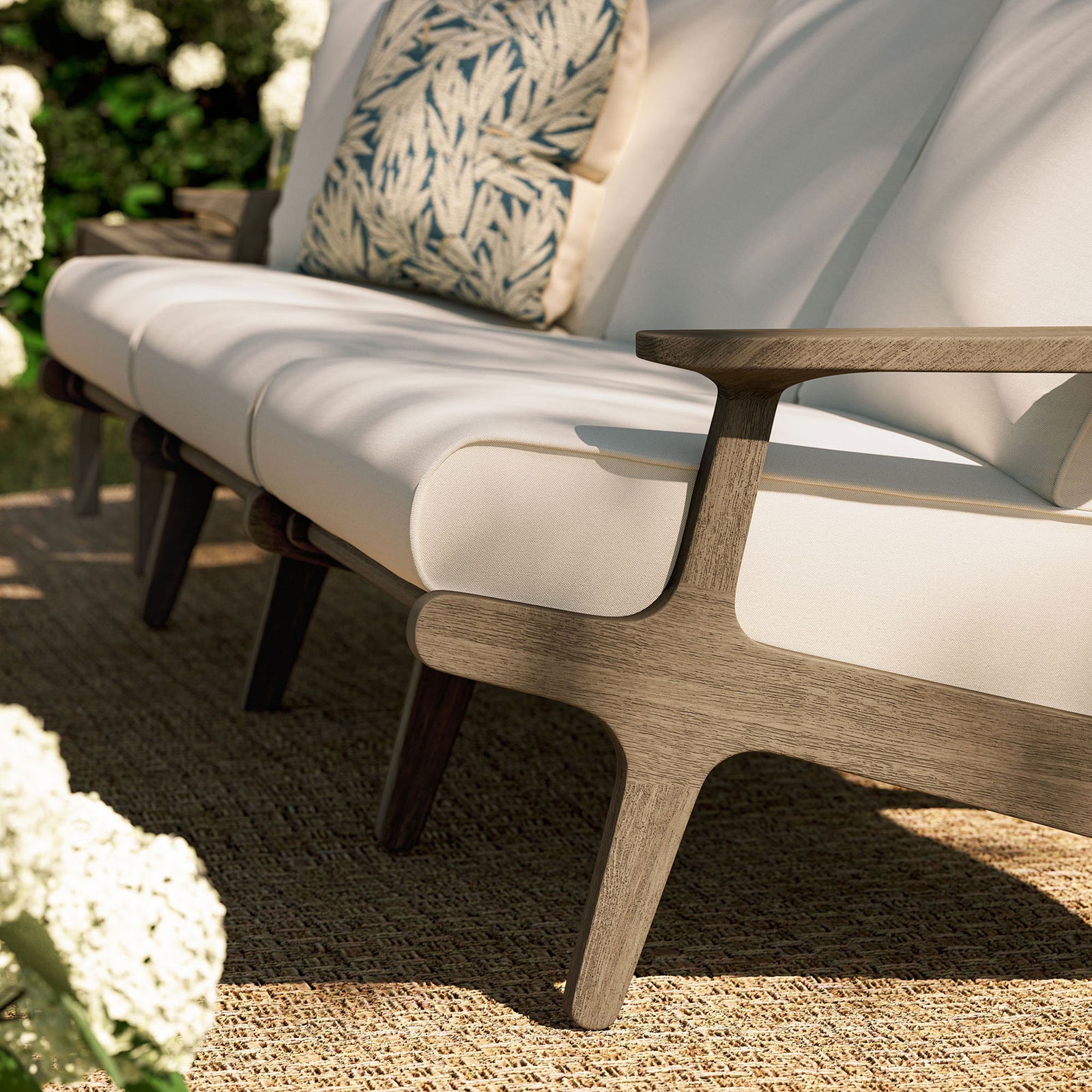 Teak sofa base with white cushions on woven outdoor rug surrounded by blooming garden plants || EEI-7249-WGR-WHI || detail_room