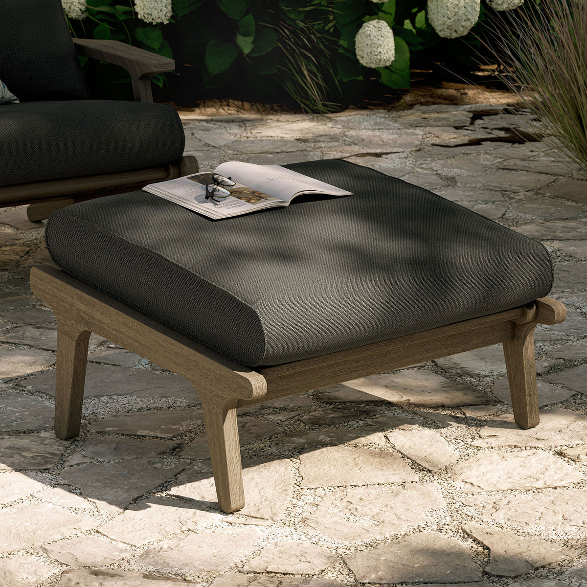 Flint gray cushioned teak ottoman styled outdoors as a chic footrest and extra patio seating || EEI-7250-WGR-FLI || front_angle_room