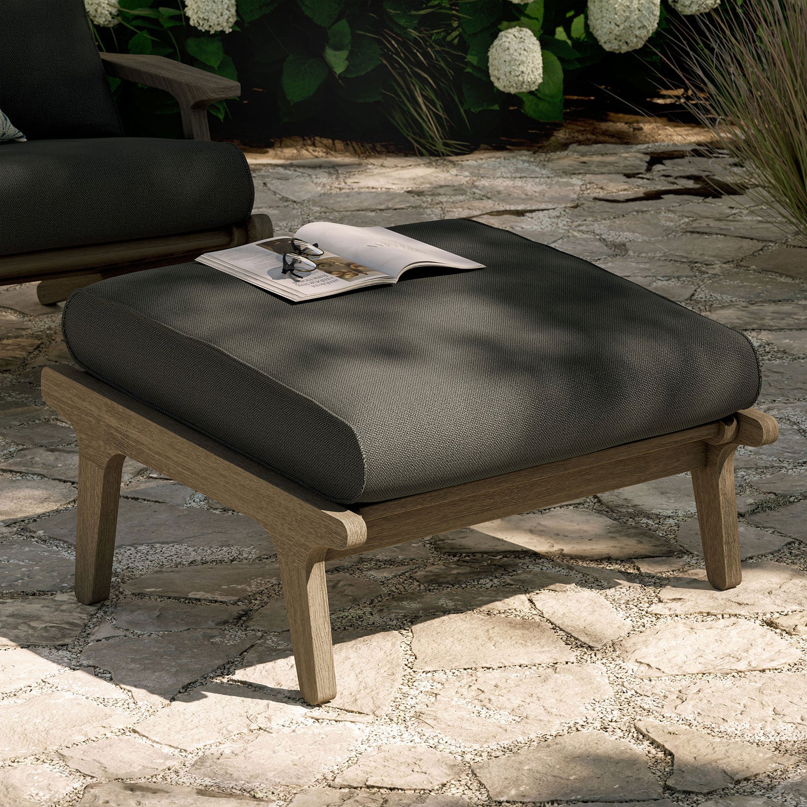 Flint gray cushioned teak ottoman styled outdoors as a chic footrest and extra patio seating || EEI-7250-WGR-FLI || front_angle_room