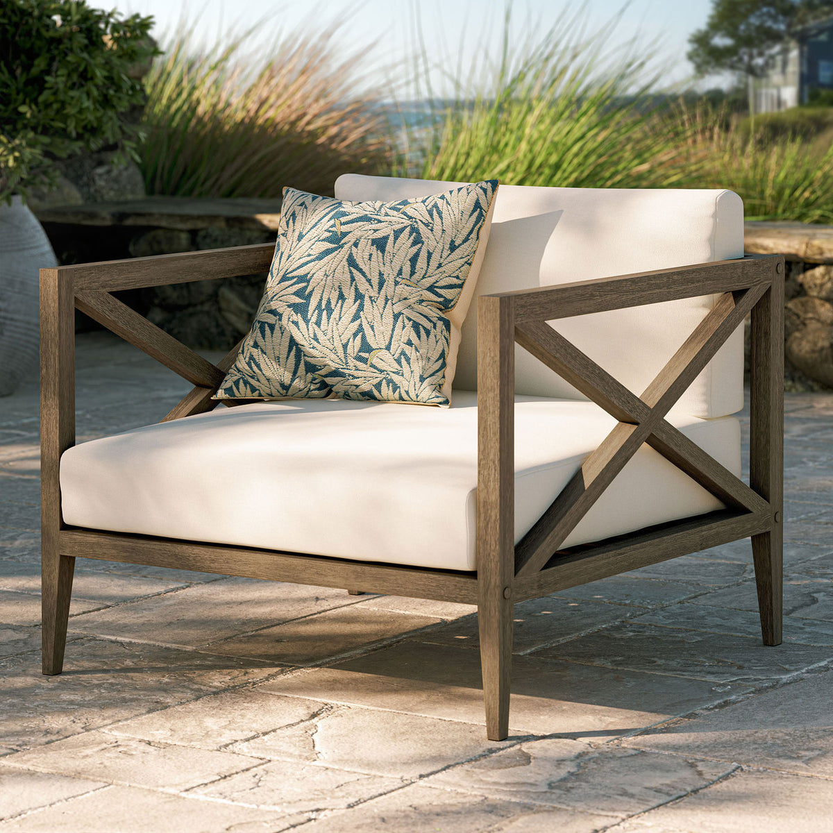 Northlake teak armchair with white cushions and a leafy accent pillow set on a sunwashed stone patio || EEI-7252-WGR-WHI || front_angle_room
