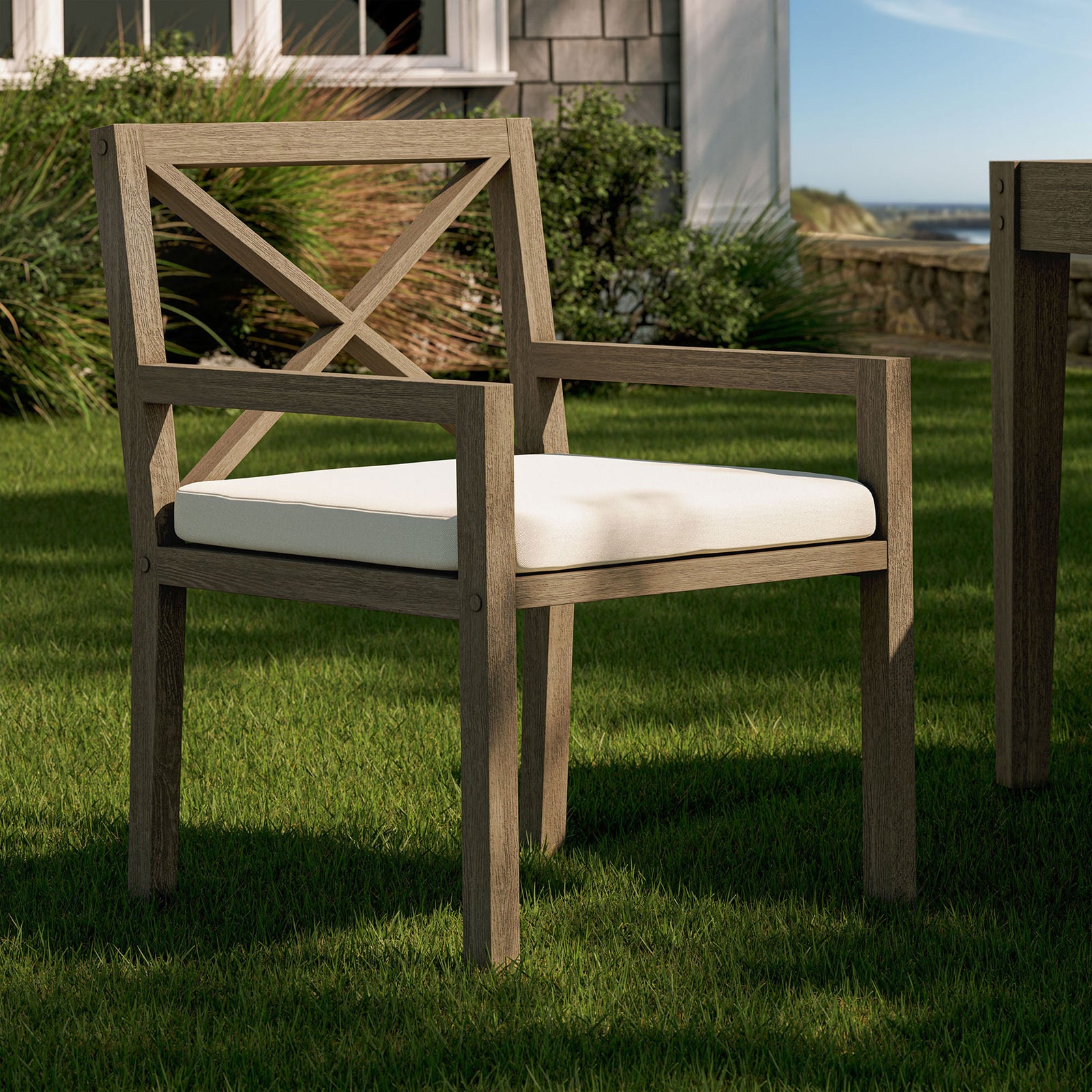 Northlake teak armchair with white cushion placed on a lush lawn beside an inviting outdoor table. || EEI-7253-WGR-WHI || front_angle_room