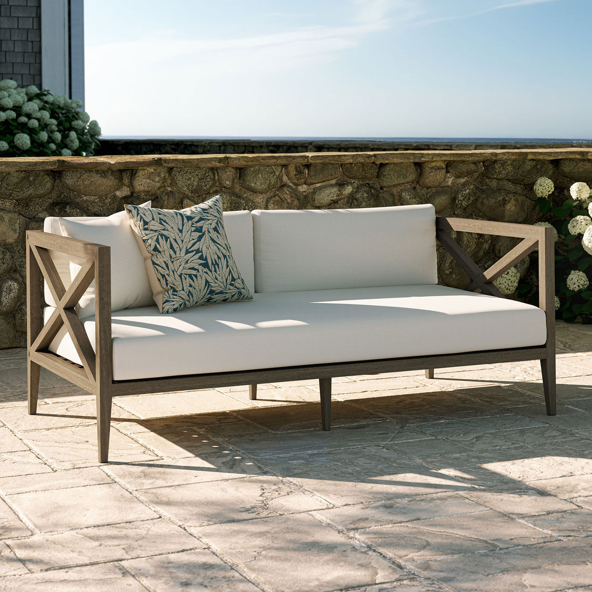 White cushioned teak loveseat styled on a stone patio, perfect for garden lounges and coastal decks. || EEI-7254-WGR-WHI || front_angle_room