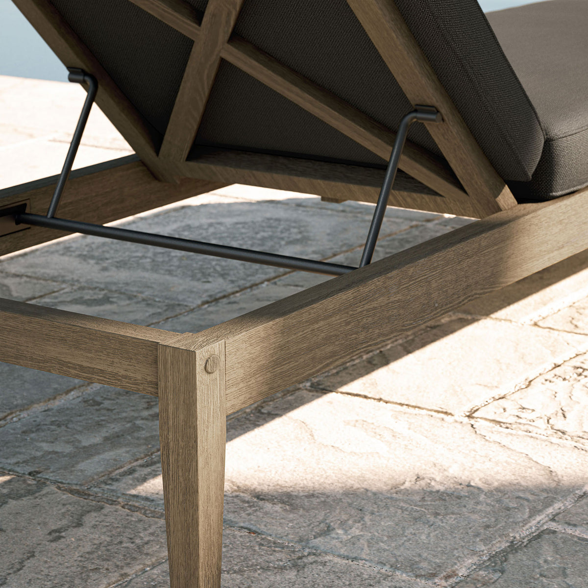 Weathered teak frame and dark gray cushion detail shown beside a sunlit stone poolside patio || EEI-7256-WGR-FLI || detail_room