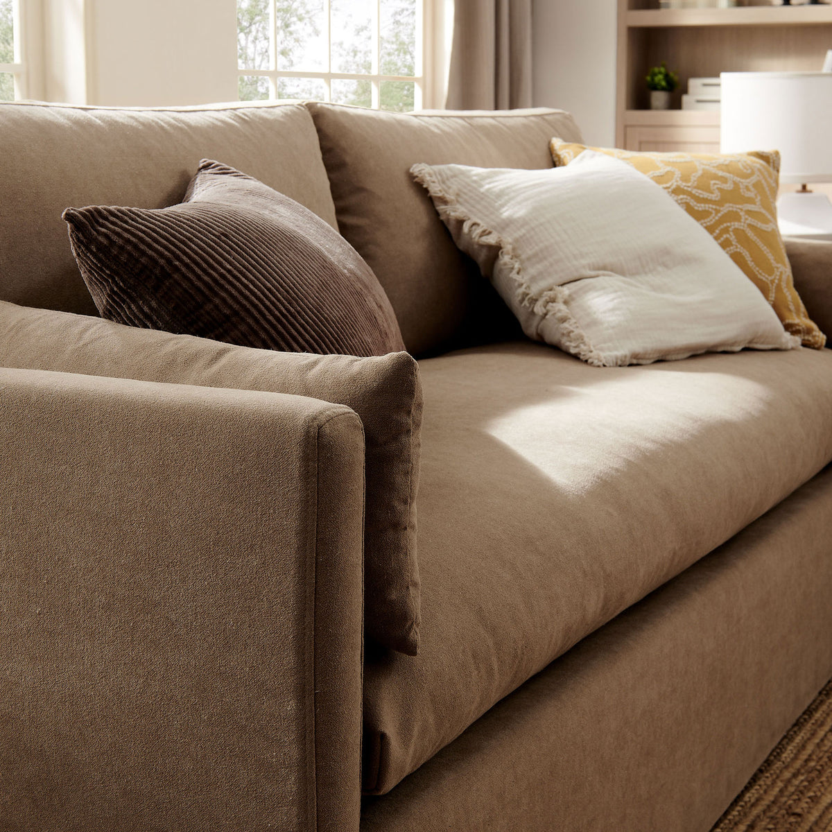 Almond slipcovered sofa seat with layered textured throw pillows creating a cozy, inviting lounge spot. || EEI-7260-ALM || detail_room