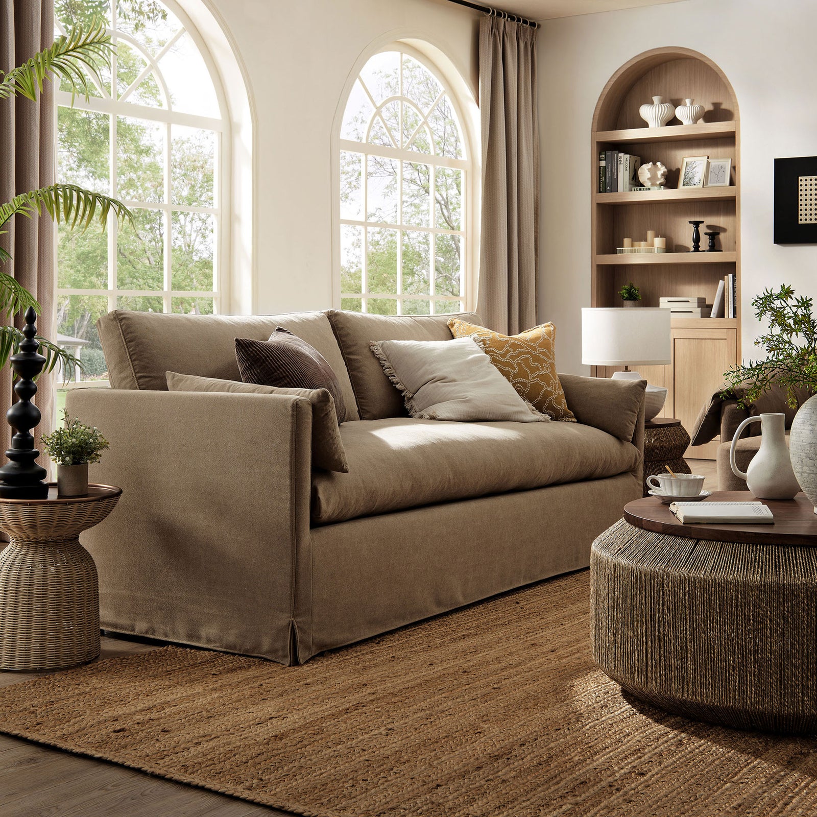 Almond slipcovered sofa styled in a bright living room with layered throw pillows and natural textures. || EEI-7260-ALM || front_angle_room