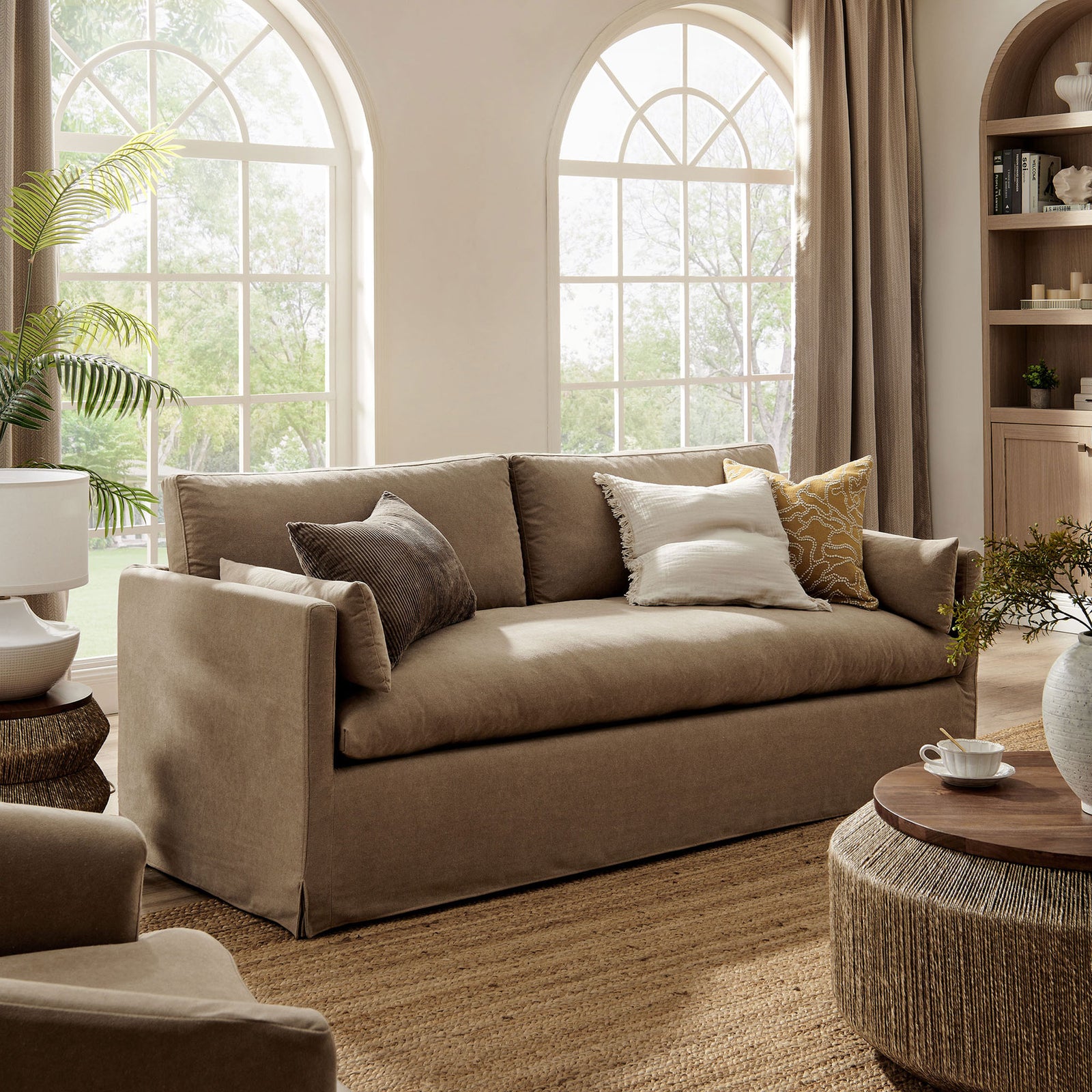 Casual almond sofa with slipcover, plush bench cushion, and accent pillows in a sunlit living space. || EEI-7260-ALM || front_angle_room