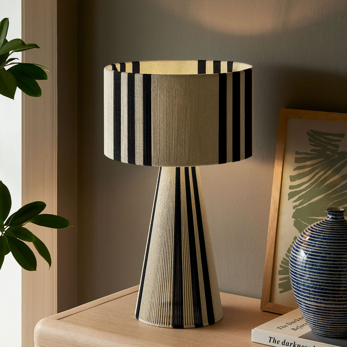 Black striped table lamp softly illuminated for an inviting nighttime glow. || EEI-7262-BLK || front_angle_on_room