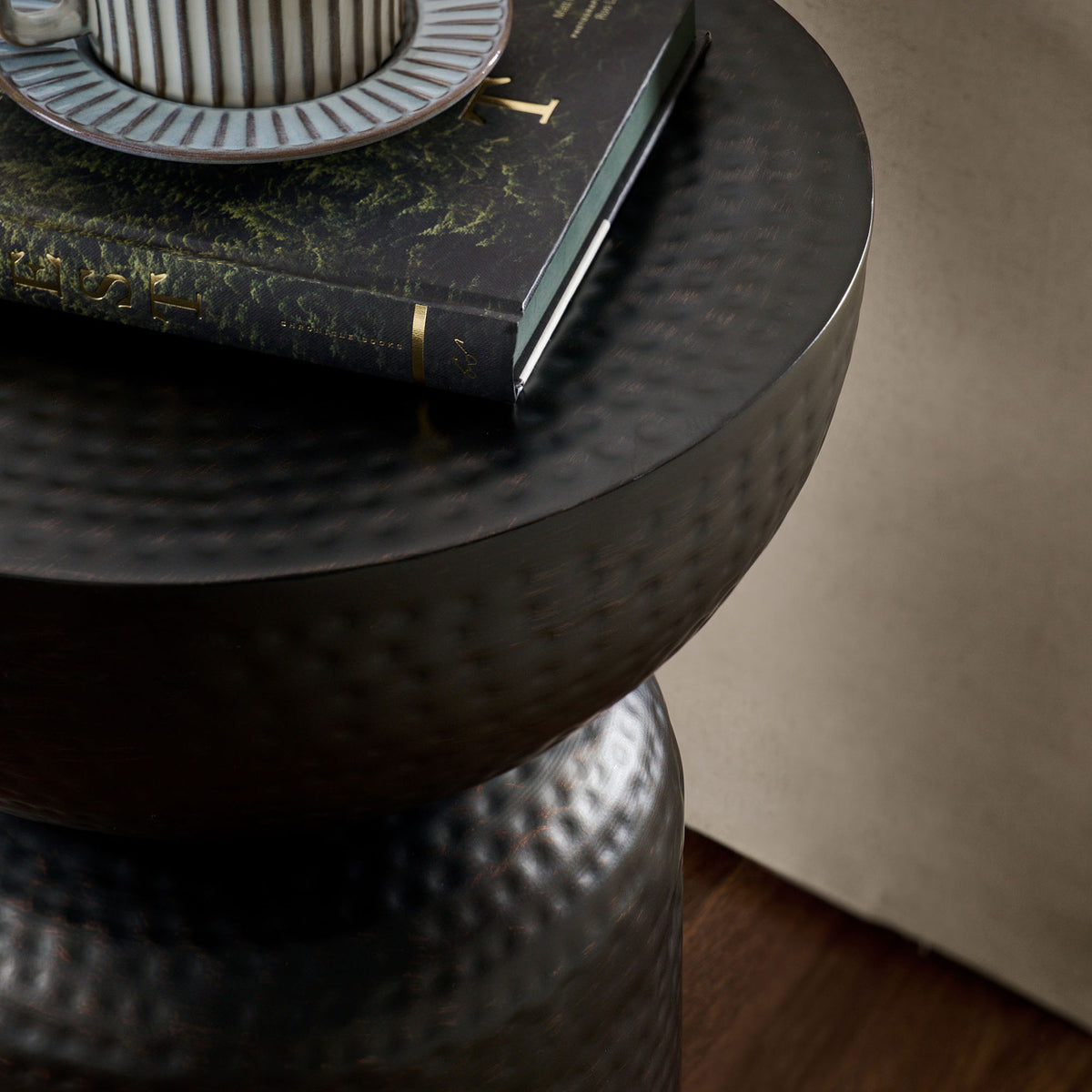 Hammered black metal tabletop styled with a striped mug and book on warm wood flooring || EEI-7278-BLK || detail_room