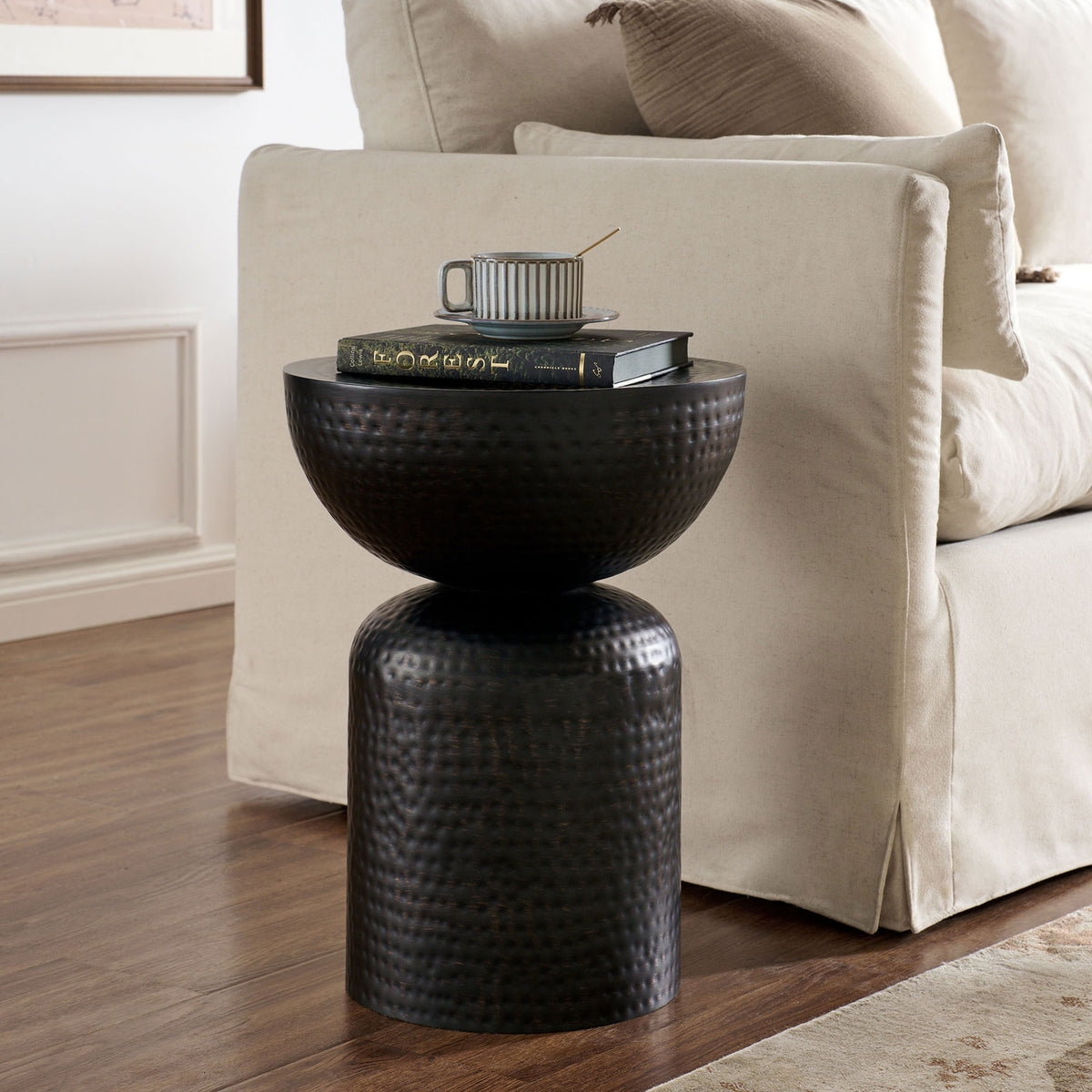 Black hammered metal pedestal side table adding sculptural contrast beside a neutral sofa || EEI-7278-BLK || front_angle_room