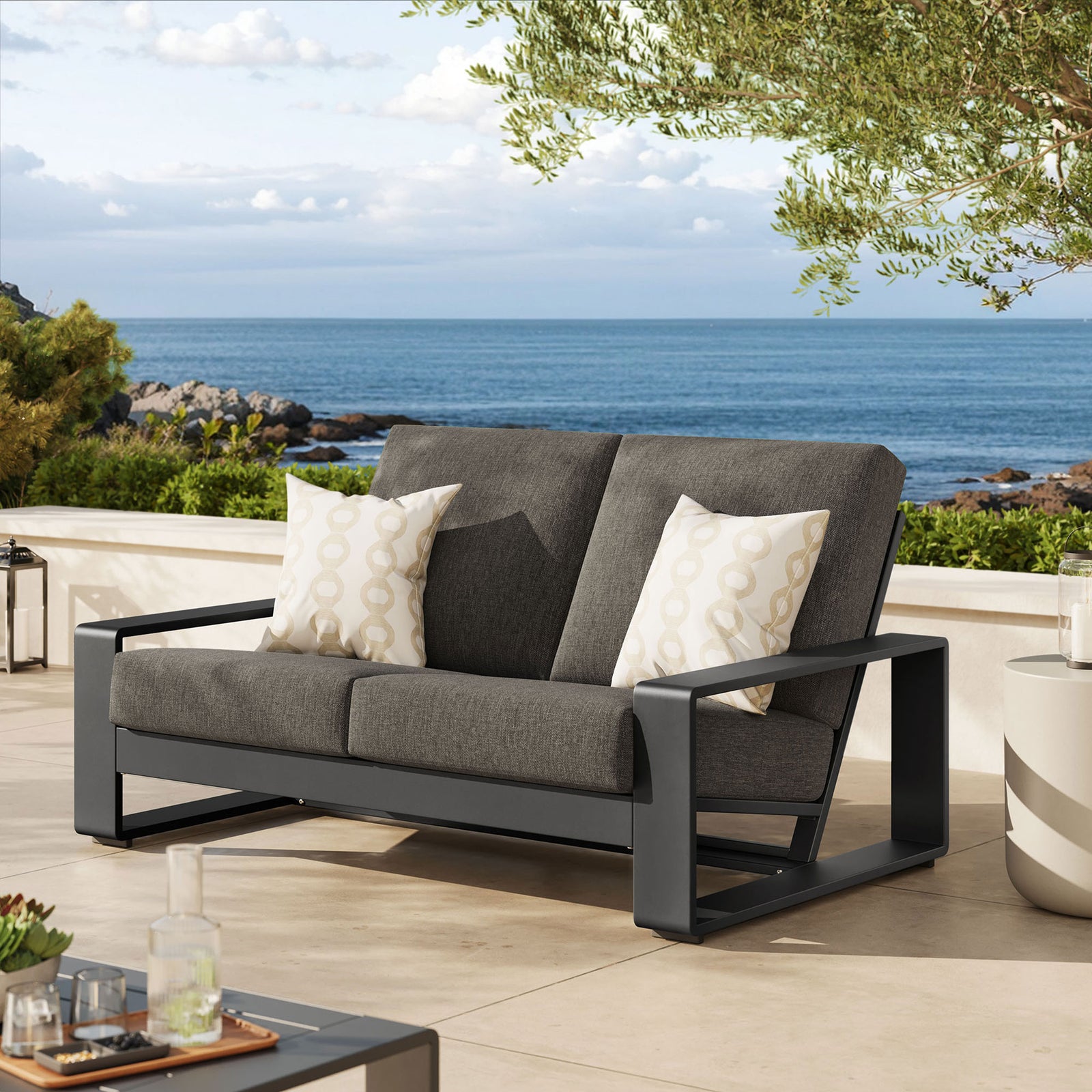 Smoke gray loveseat with charcoal frame brings sophisticated comfort to a sunlit terrace setting || EEI-7301-SMO-GRY || front_angle_room