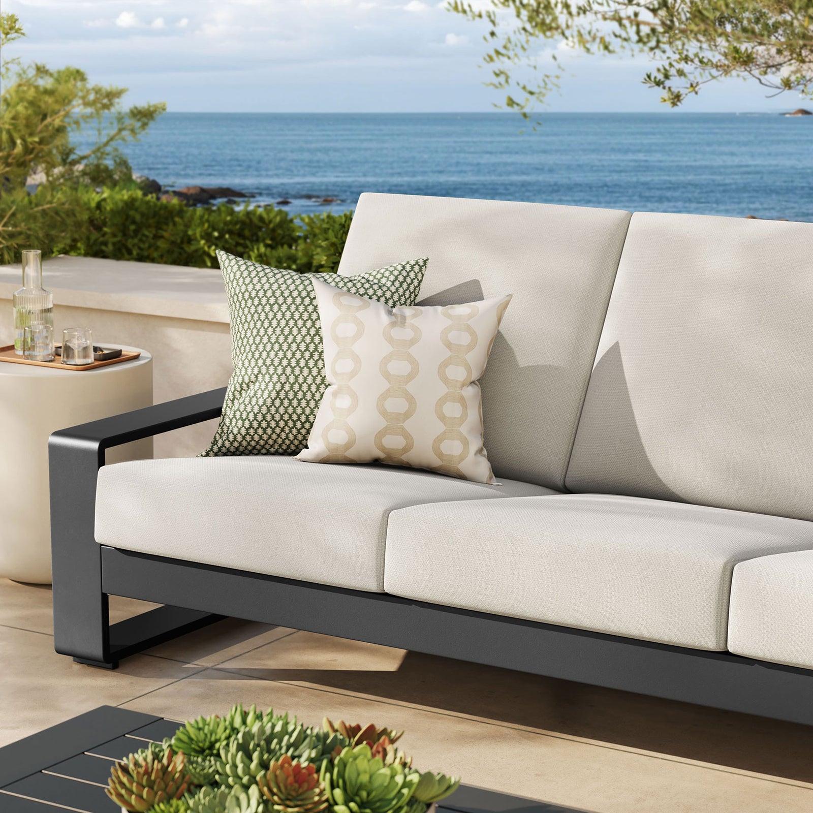 Cream outdoor sofa styled with patterned pillows, adding soft contrast against the dark aluminum base || EEI-7302-CRE-GRY || detail_room