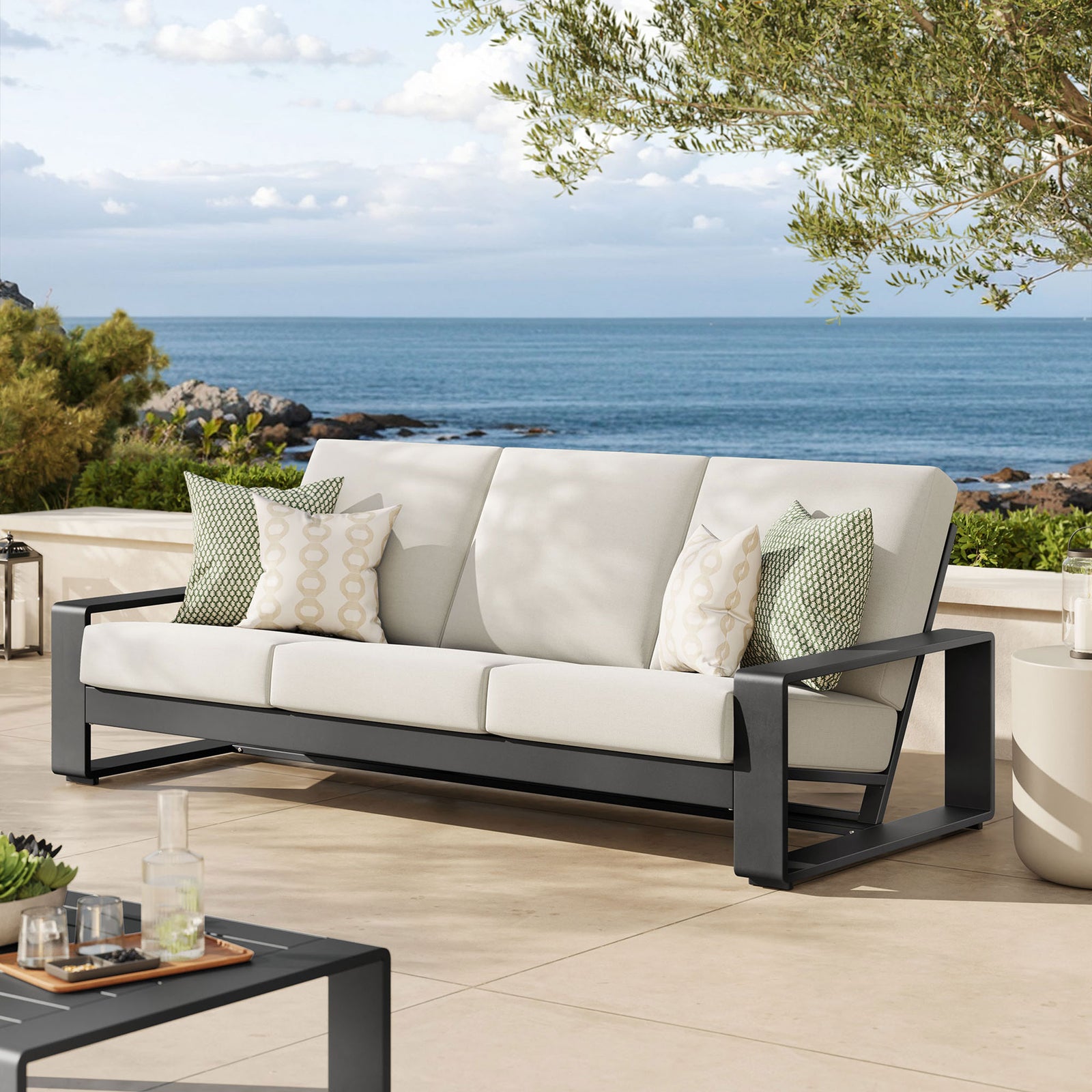 Cream three-seat outdoor sofa on a coastal patio, pairing plush cushions with a strong charcoal aluminum frame || EEI-7302-CRE-GRY || front_angle_room
