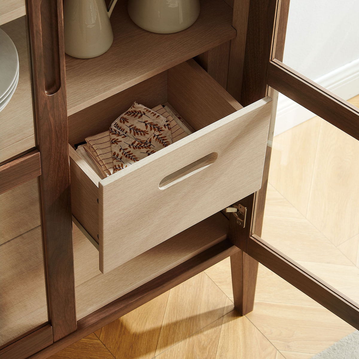 Open drawer of the Nell tall cabinet neatly storing serveware and linens for convenient dining room organization || EEI-7320-WAL-ASH || storage_open_room