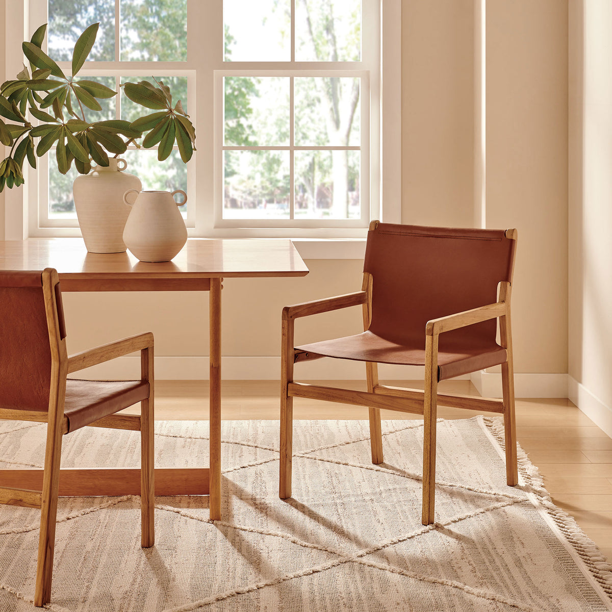 Pair of Sonora leather dining chairs around a teak table in a bright, welcoming dining room || EEI-7325-CSN || front_angle_room
