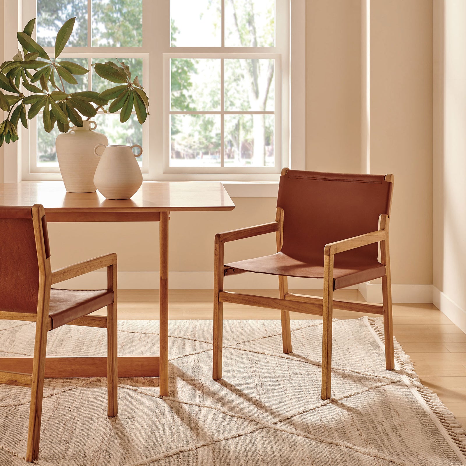 Pair of Sonora leather dining chairs around a teak table in a bright, welcoming dining room || EEI-7325-CSN || front_angle_room