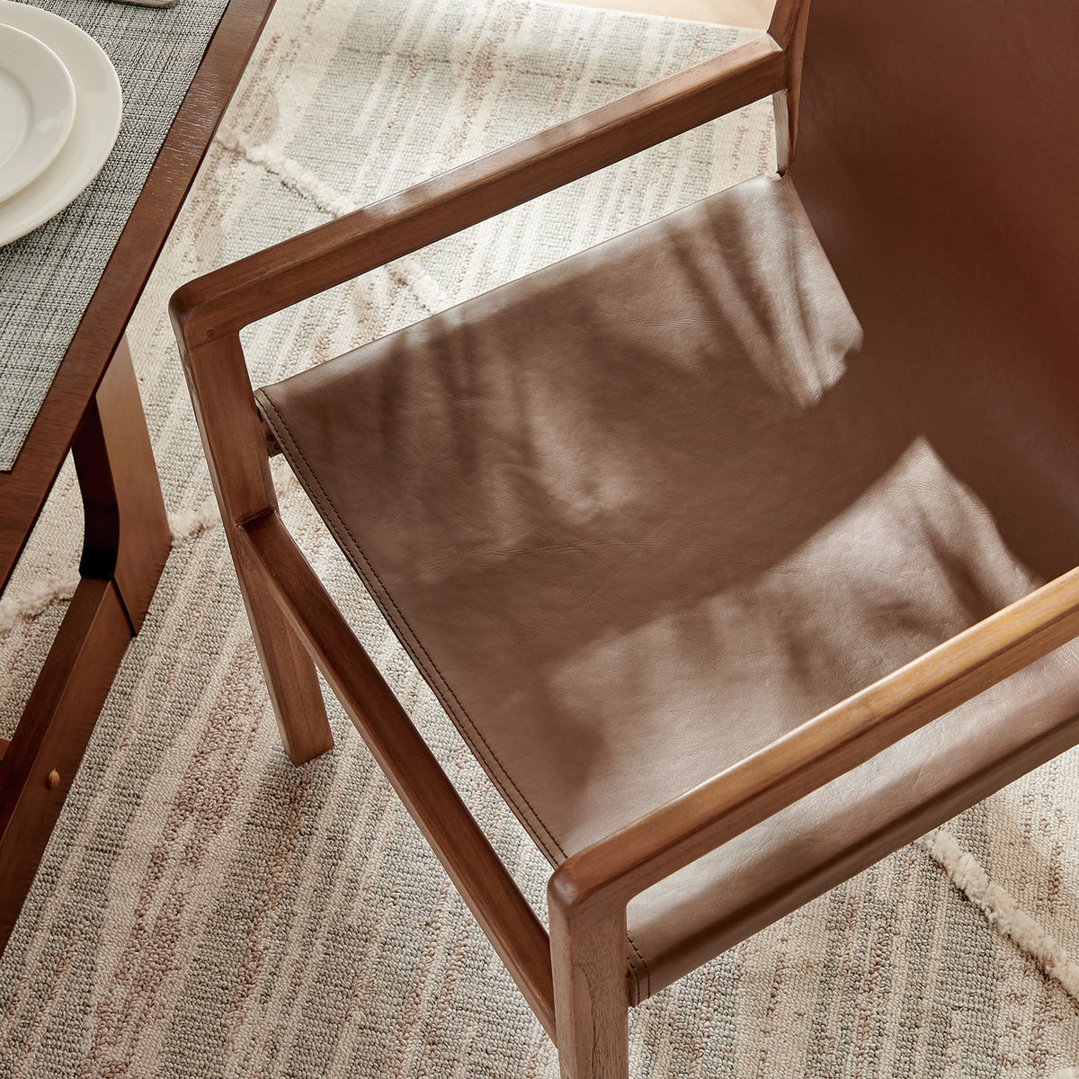 Sunlit nutmeg brown leather seat and teak frame at the dining table, highlighting rich texture. || EEI-7325-NUT || detail_room