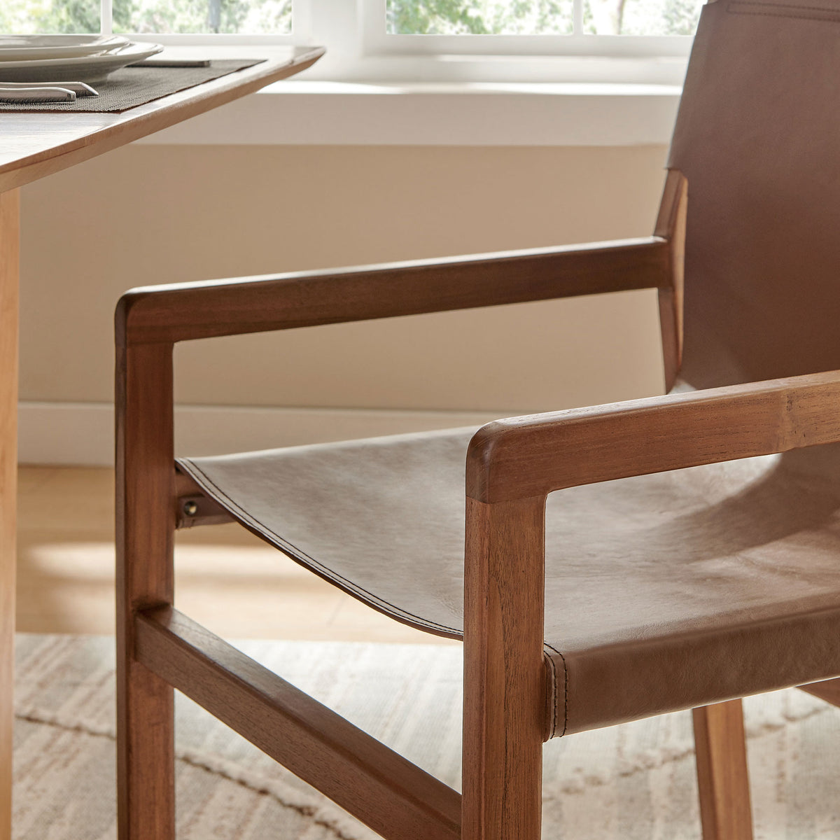 Teak armrest and leather sling seat of Sonora chair styled beside a modern dining table. || EEI-7325-NUT || detail_room