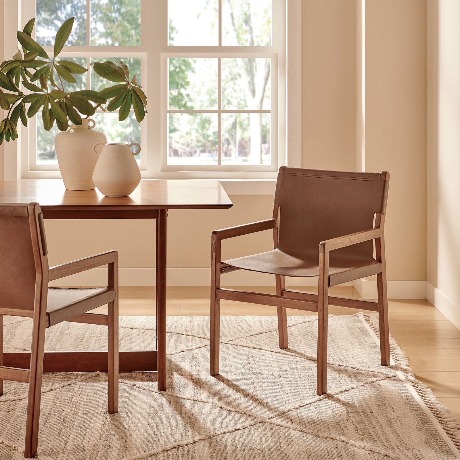 Pair of Sonora nutmeg brown leather dining chairs around a wood table on a neutral rug. || EEI-7325-NUT || front_angle_room
